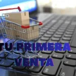 Carrito de compras con paquete sobre un teclado de computadora, representando una primera venta en una tienda online.