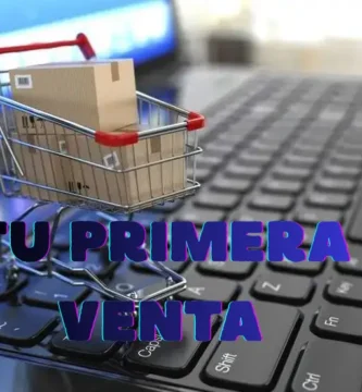 Carrito de compras con paquete sobre un teclado de computadora, representando una primera venta en una tienda online.